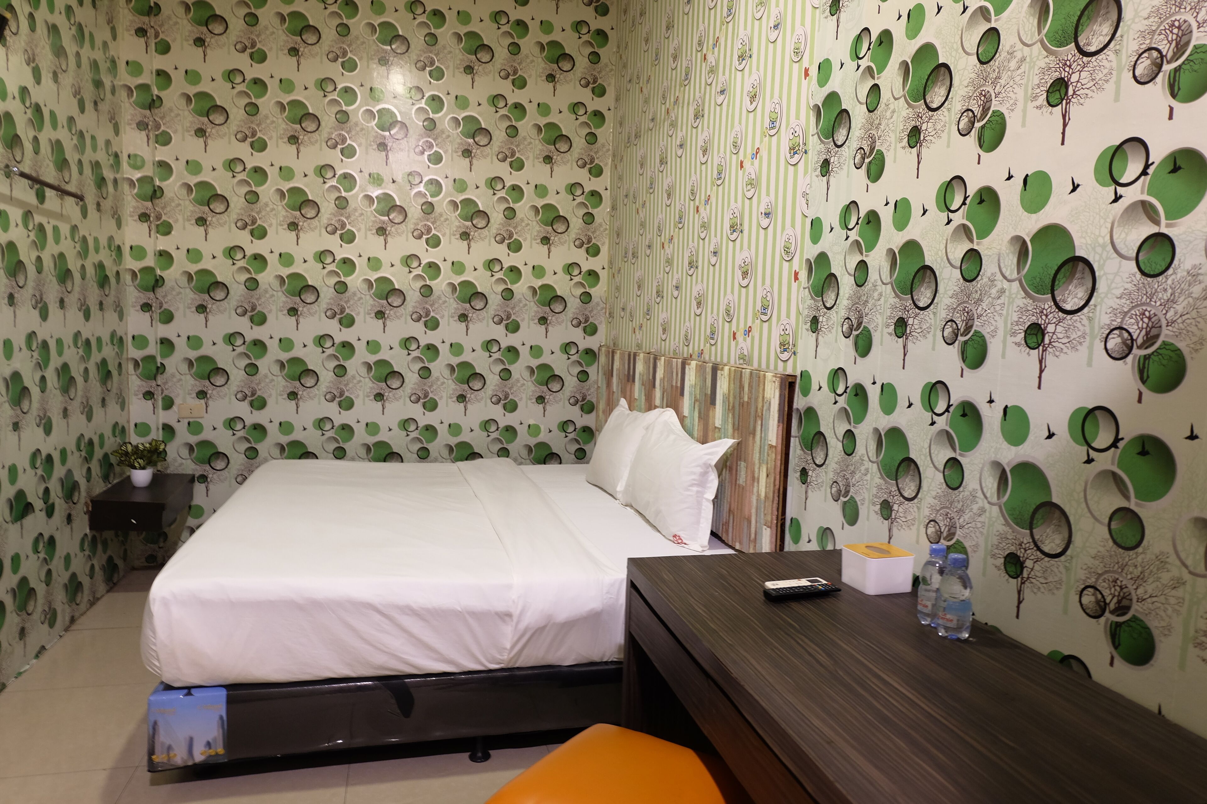A hotel room with a bed, a desk, and a chair. There are two bottles on the desk.