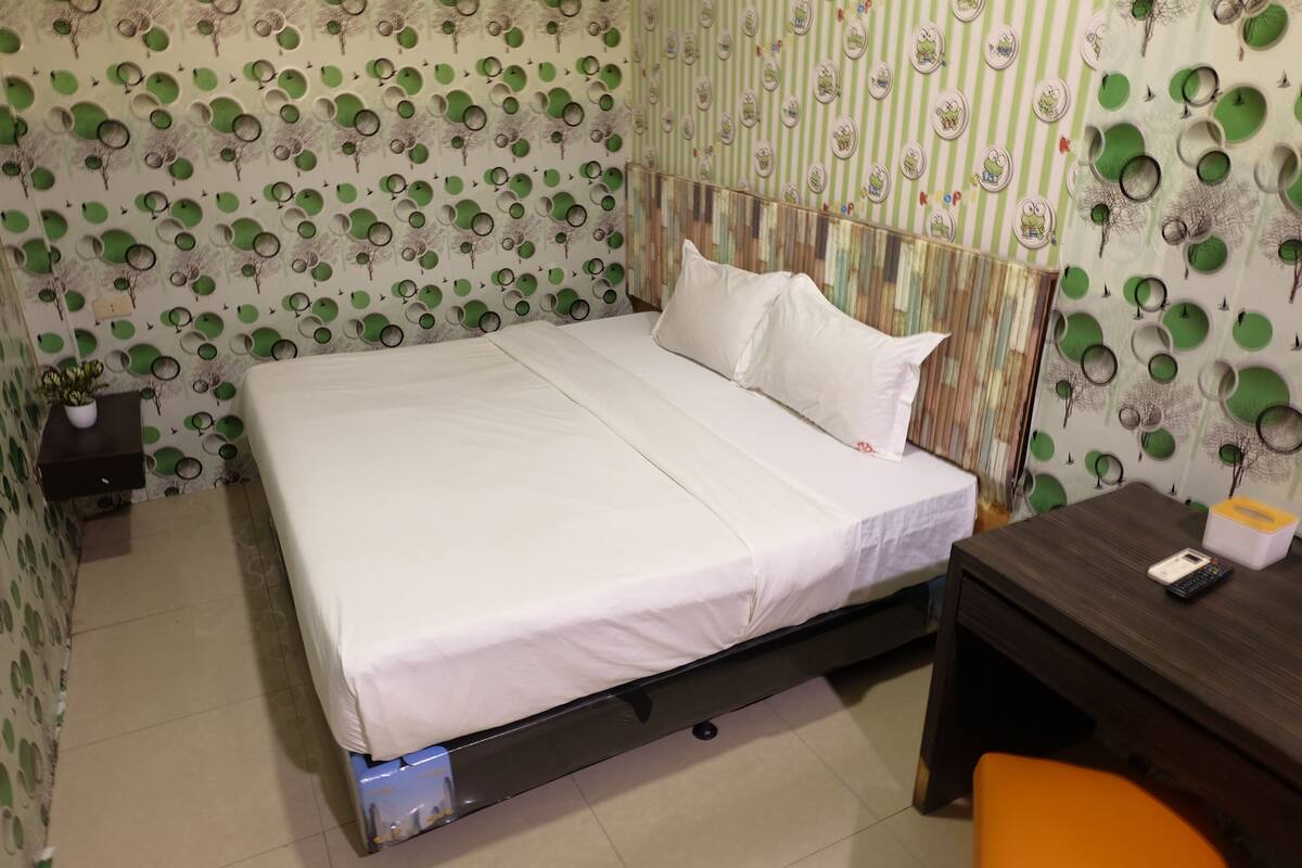 Ein ordentlich bezogenes Bett mit weißen Leinen in einem Zimmer mit ornamentalem Wandpapier und einem Holzkopfteil.