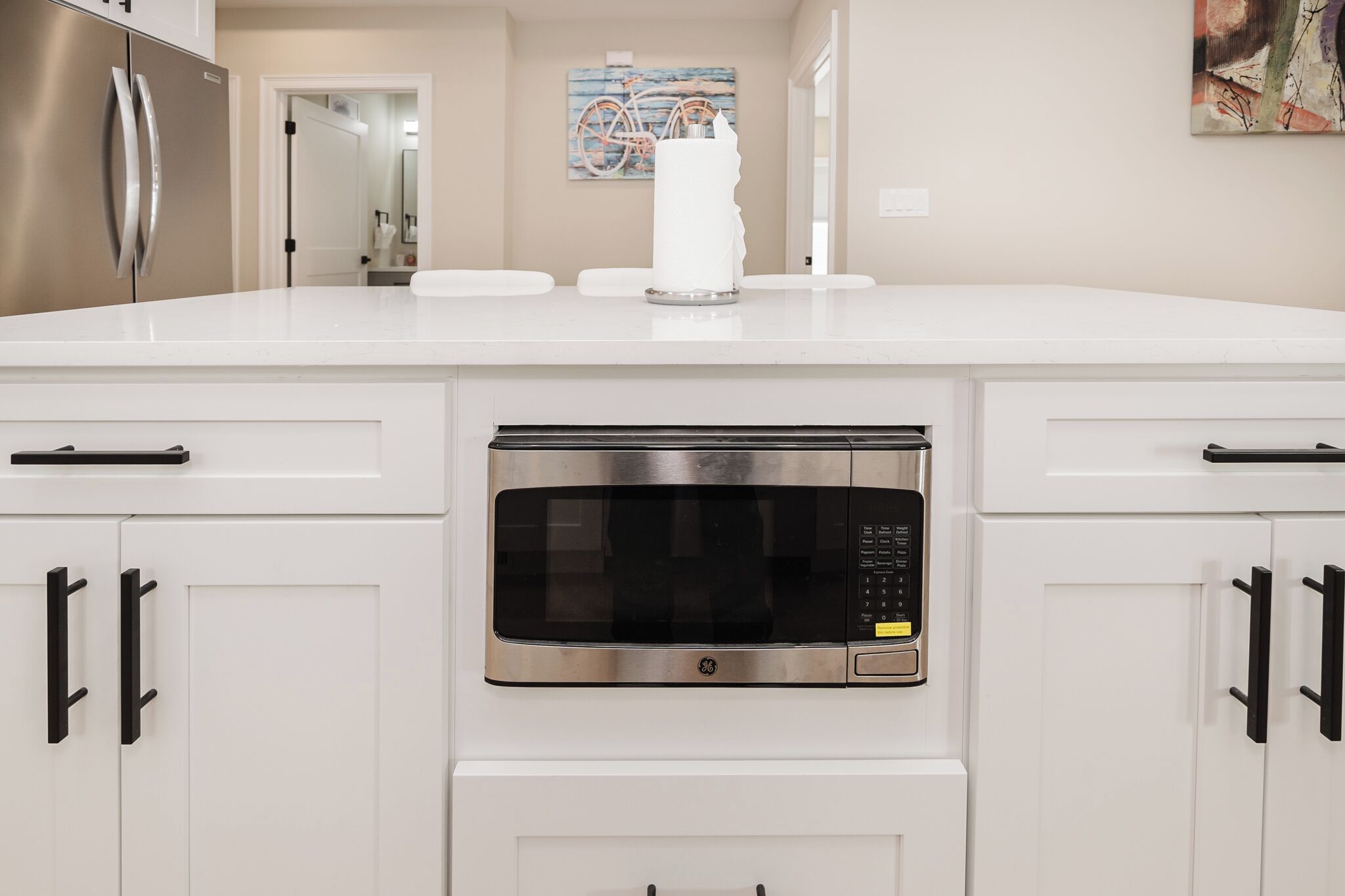 A kitchen with white cabinets, a stainless steel microwave, and a white countertop.