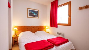 Un letto matrimoniale con coperte rosse, due lampade ai lati, una testiera in legno, una finestra con tende rosse e un quadro appeso al muro.