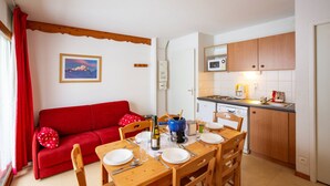 Un ambiente compatto con angolo ristoro, un divano rosso, una cucina con forno a microonde e un quadro appeso al muro.