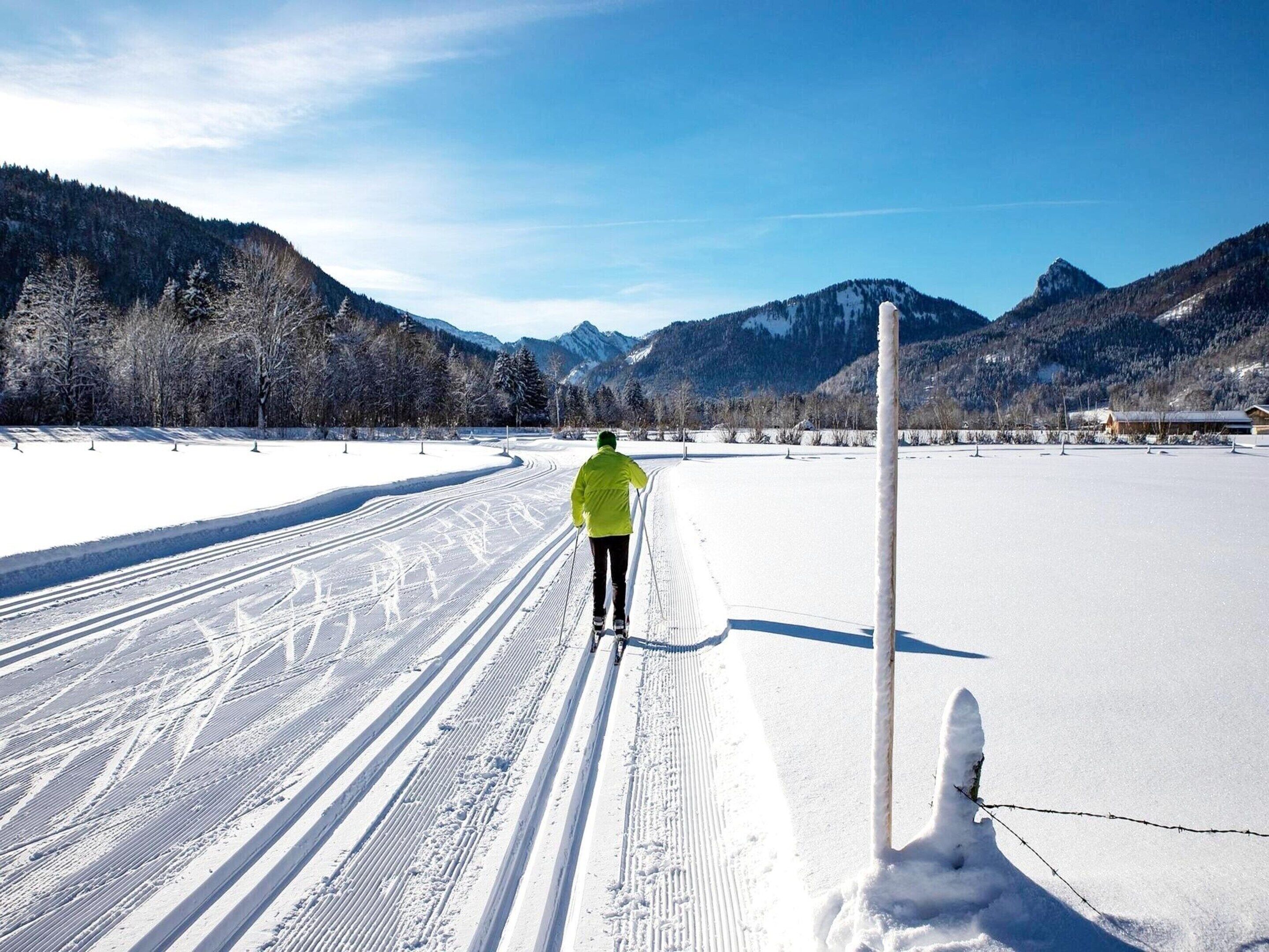 A cross-country skier on a snowy trail with mountains in the background.