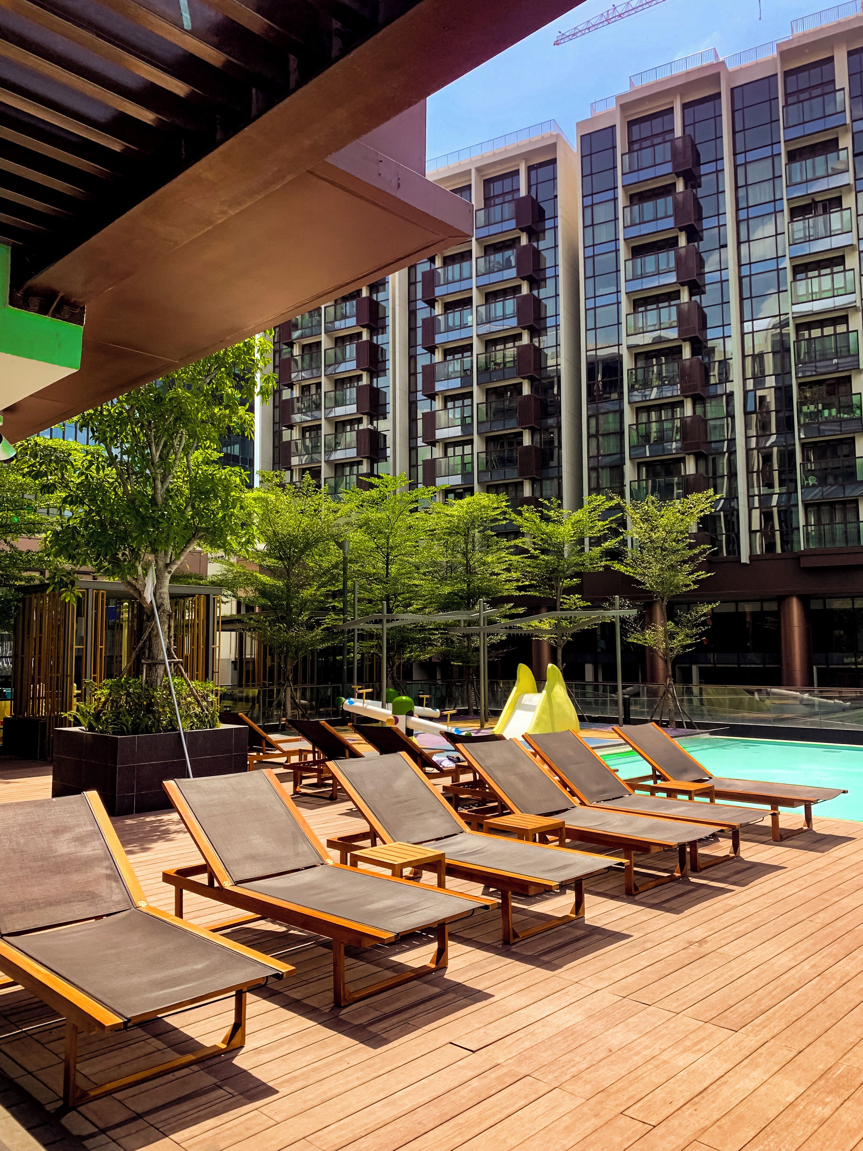 Zona de piscina en la azotea con sillones de sol y vistas a un edificio moderno con balcones.