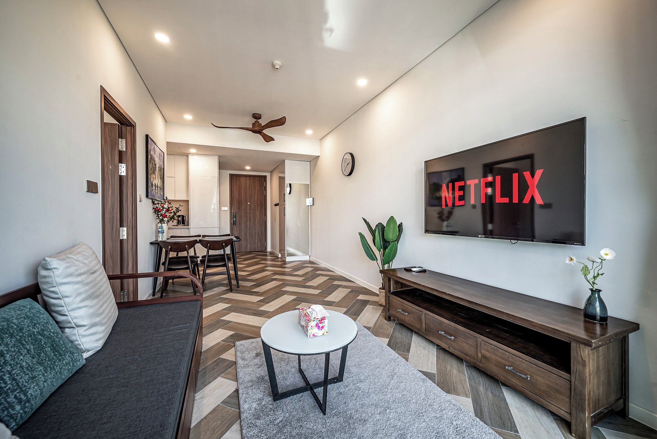 A modern living room with a sofa, a coffee table, a TV, and a dining area.