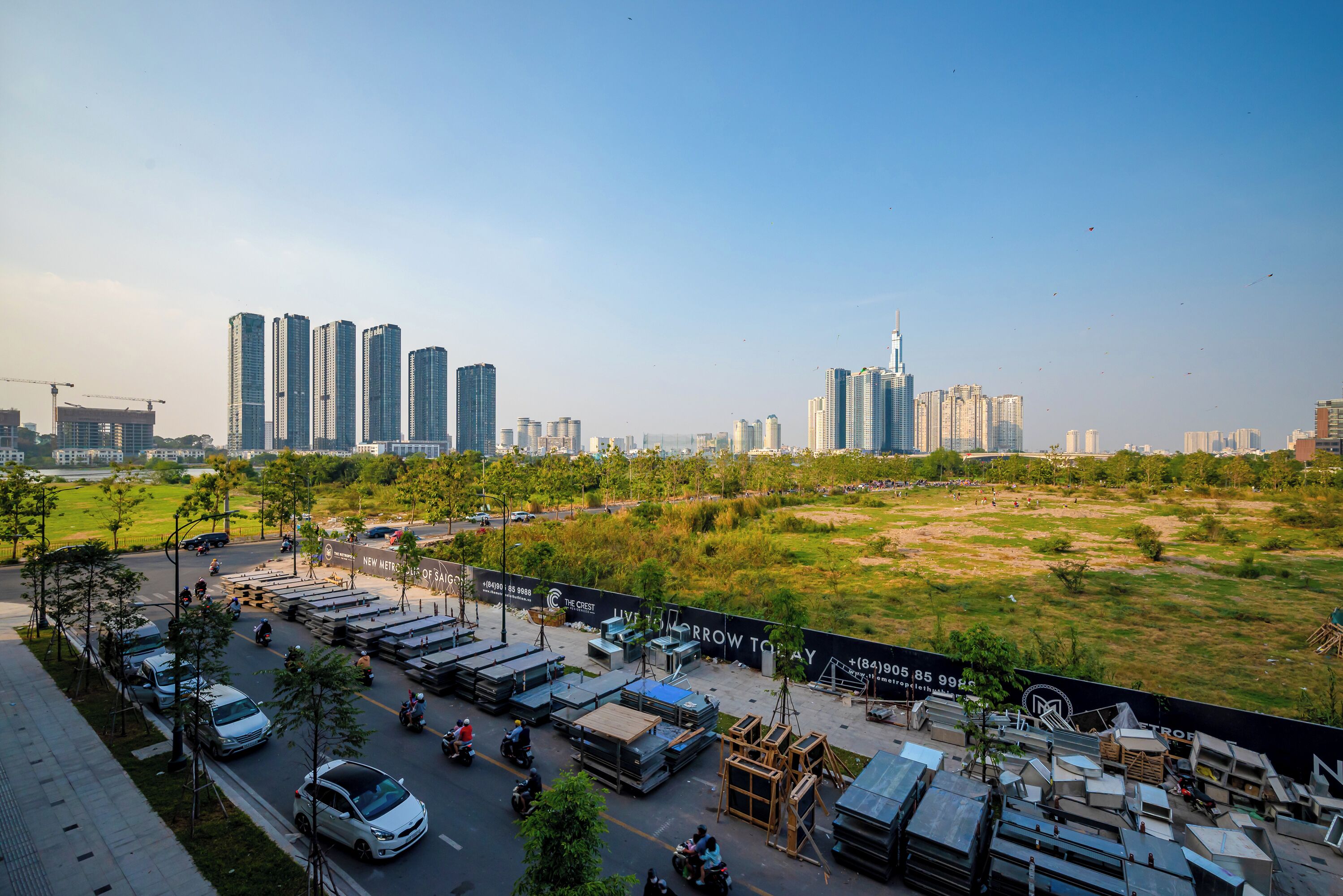 Ein Parkplatz mit Autos und Motorrädern, umgeben von Baumaterialien und einem grünen Feld.