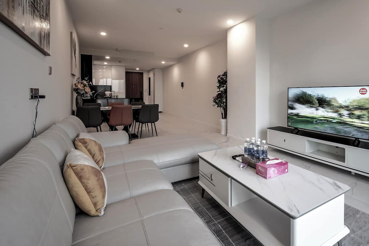 A modern living room with a sectional sofa, a flat-screen TV, and a dining area in the background.