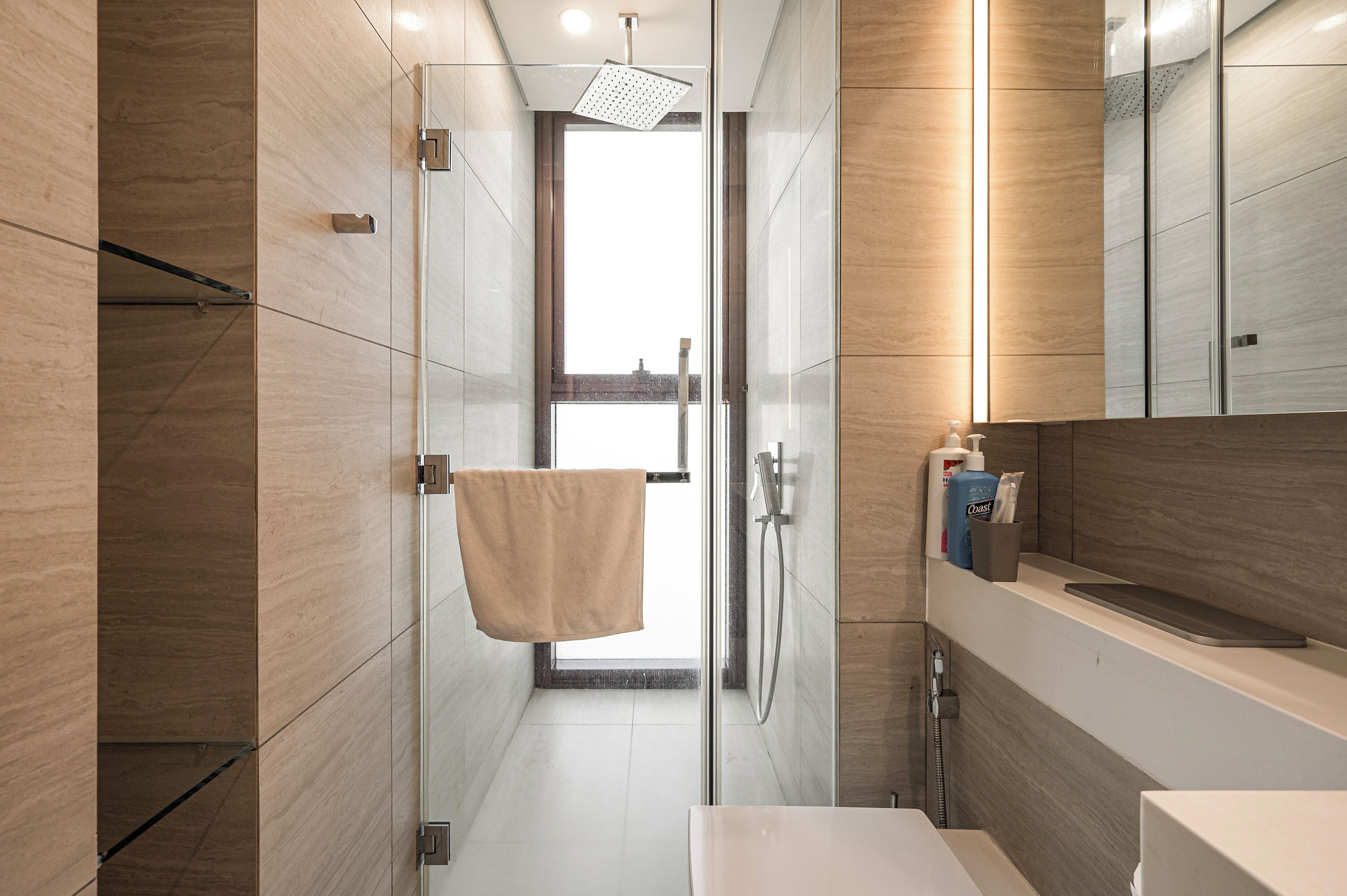 A modern bathroom with a glass shower enclosure, a towel hanging on the wall, and a shelf with toiletries.