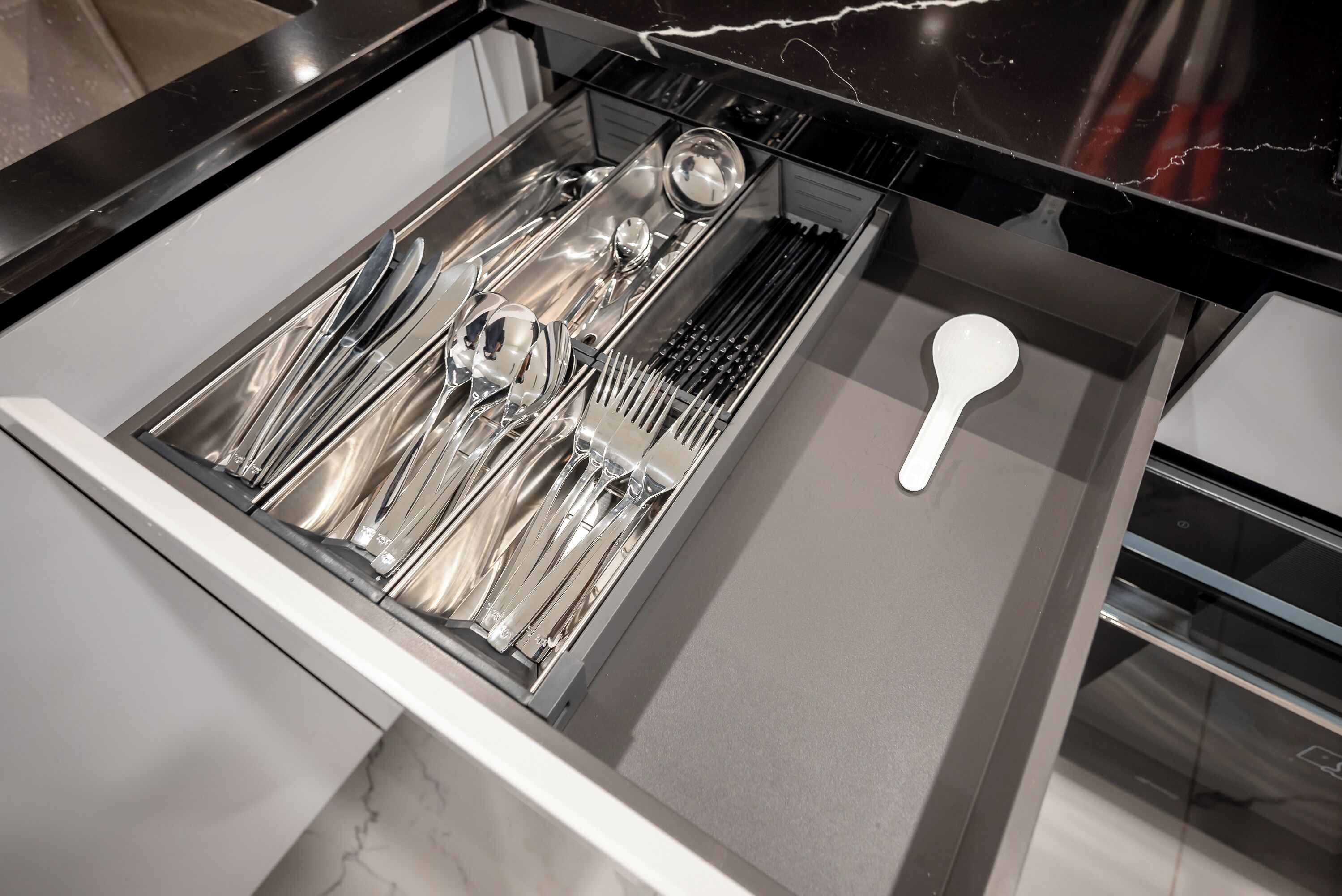 Un cajón de cocina con utensilios y una cuchara blanca.