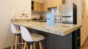 Una cocina moderna con encimera de granito, refrigerador de acero inoxidable y dos taburetes blancos.