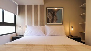 Habitación de hotel con una cama grande, dos mesitas de noche con lámparas, un ventanal y un cuadro en la pared.