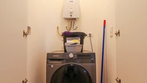 Un lavadero equipado con lavadora y secadora Samsung, un trapeador y un sistema de ventilación.