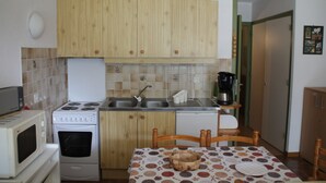 Eine kleine Küche mit Holzschränken, einem Herd, einer Mikrowelle, einem Spülbecken und einer Kaffeemaschine.