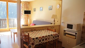 Ein gemütliches Zimmer mit Esstisch, Stühlen, einer Couch, einem Fernseher, einer Mikrowelle und einem Fenster mit Blick auf Bäume.