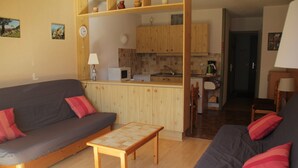 Ein gemütliches Wohnzimmer mit einer Couch, einem kleinen Holztisch und einer Küchenzeile mit Holzschränken und einer Mikrowelle.