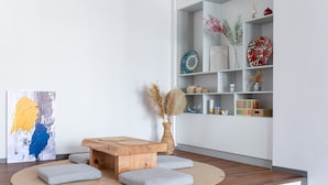 Een moderne woonkamer met een houten salontafel, grijze kussens, een rond vloerkleed en een boekenkast met decoratieve objecten.