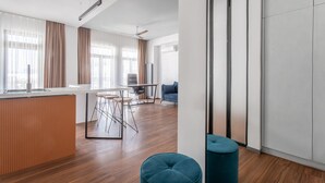 Een moderne woonkamer met houten vloer, een eethoek met tafel en stoelen, en een groot raam met gordijnen.