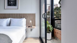 A modern bedroom with a bed, bedside table, lamp, and a large window with a view of the city. - w* | Radiant Loft w/ balcony in Chapinero (Bogotá)