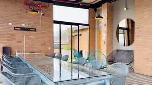 A modern meeting room with a glass table surrounded by wicker chairs, a large window, and a brick wall. - w* | Radiant Loft w/ balcony in Chapinero (Bogotá)