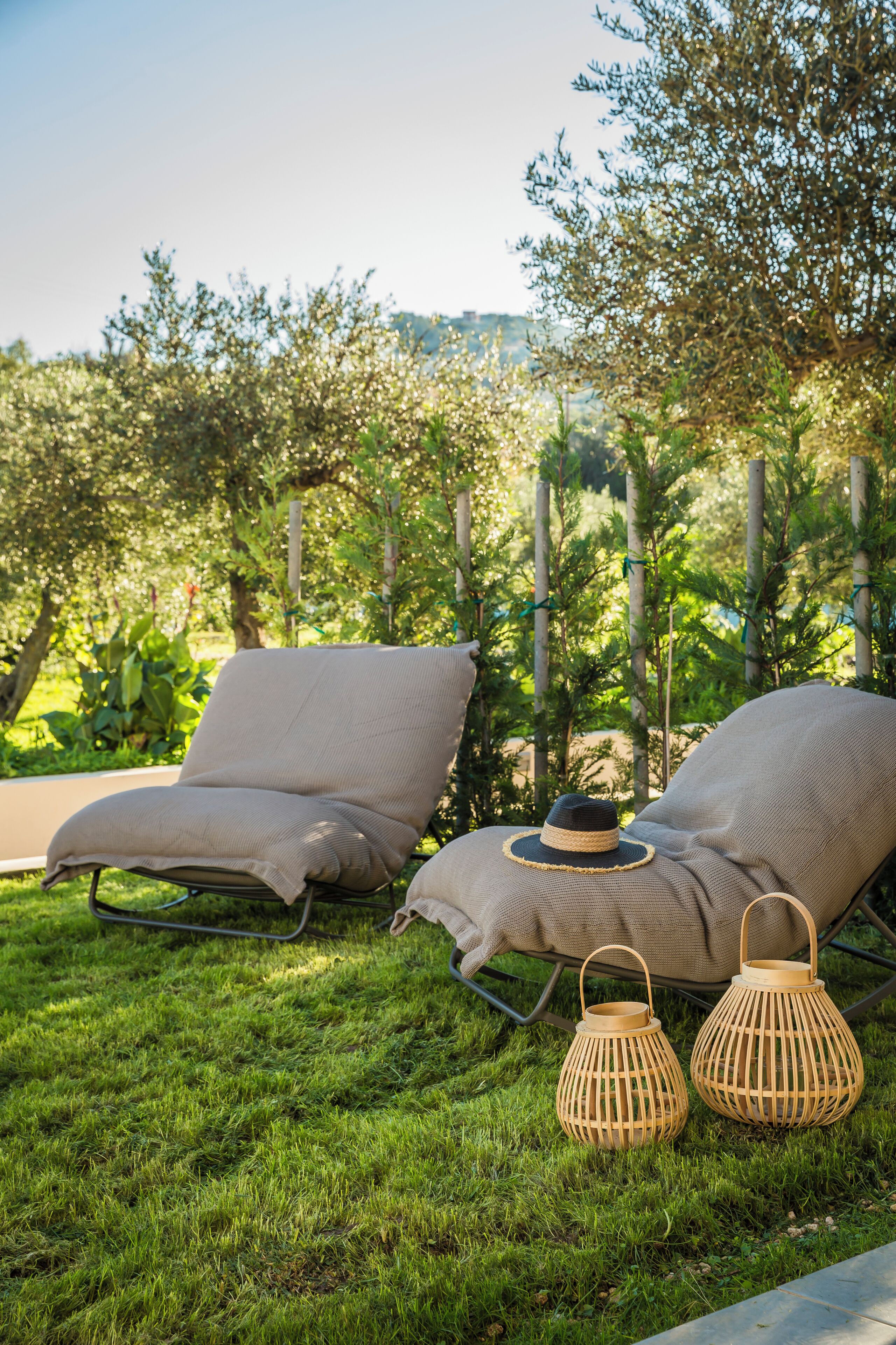 Deux fauteuils de jardin avec coussins, un chapeau et deux lanternes en osier, le tout posé sur une pelouse verdoyante, avec des arbres en arrière-plan.