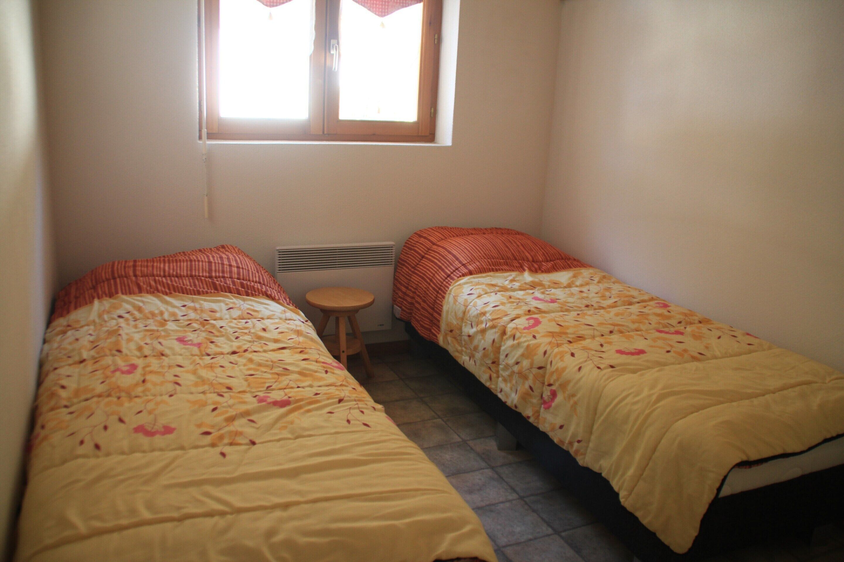 A small, single-room bedroom with two single beds, a window, and a radiator.