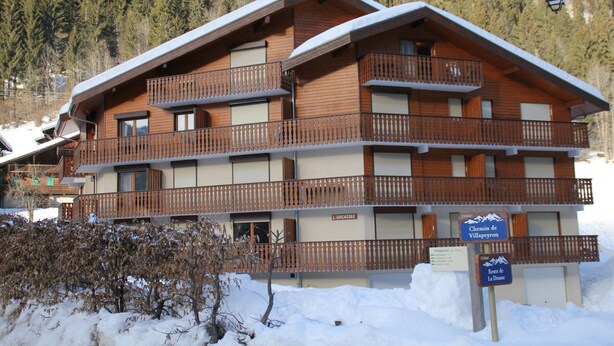 Un edificio in legno a più piani con balconi, circondato da neve e alberi.