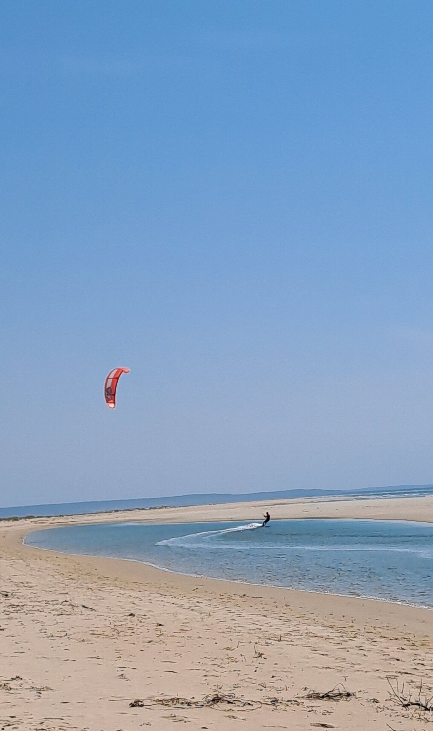 A beach with a person windsurfing.