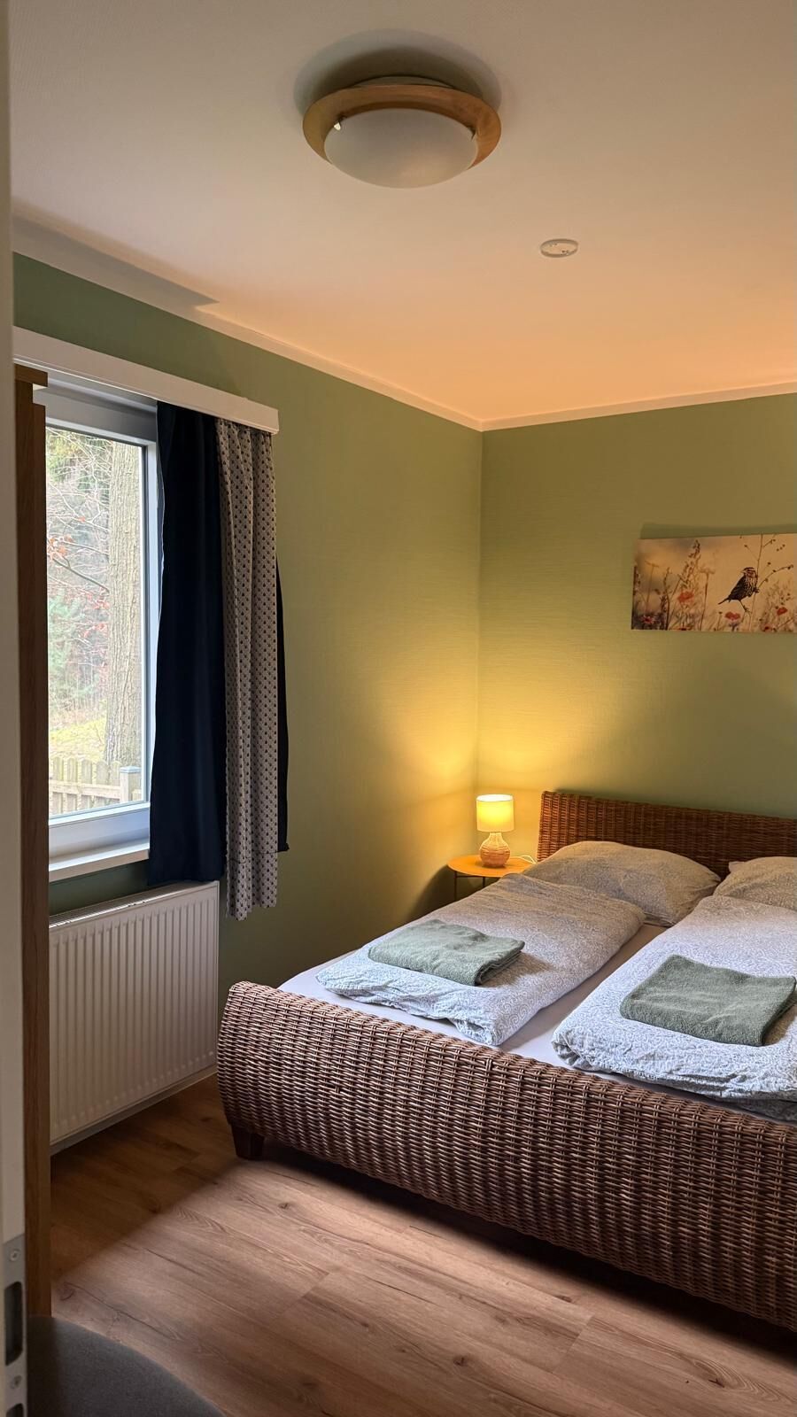 Quarto com cama, janela com cortinas, luminária na parede e um quadro.