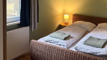 Quarto com cama, janela com cortinas, luminária na parede e um quadro.