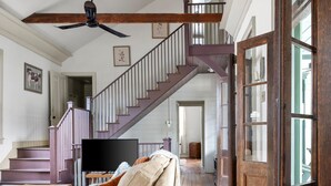 Ein geräumiges Wohnzimmer mit Holzboden, einer Couch, einem Deckenventilator und einer Treppe, die in einen oberen Bereich führt.