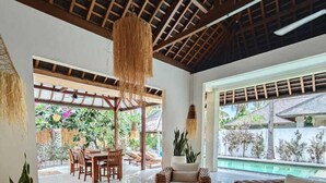 A spacious indoor area with wicker furniture, a glass coffee table, and a view of an outdoor pool area. - VILLA DUNIA (Gili Trawangan)