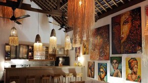 A spacious living area with wicker furniture, a bar area, and artwork on the walls. - VILLA DUNIA (Gili Trawangan)