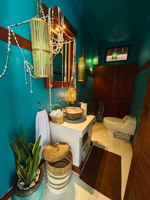 A bathroom with a white sink, a toilet, and a mirror. There are plants and baskets on the counter. - VILLA DUNIA (Gili Trawangan)
