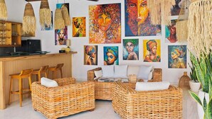 A spacious room with a high ceiling, wicker furniture, and a wall adorned with colorful paintings. - VILLA DUNIA (Gili Trawangan)