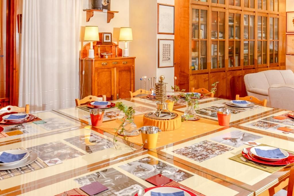 Un comedor con mesa de vidrio dispuesta para una comida, armarios de madera y cuadros en la pared.