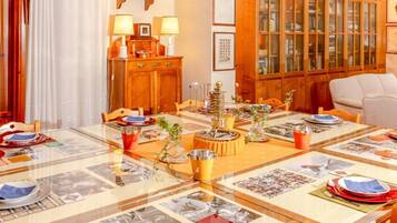 Un comedor con mesa de vidrio dispuesta para una comida, armarios de madera y cuadros en la pared.