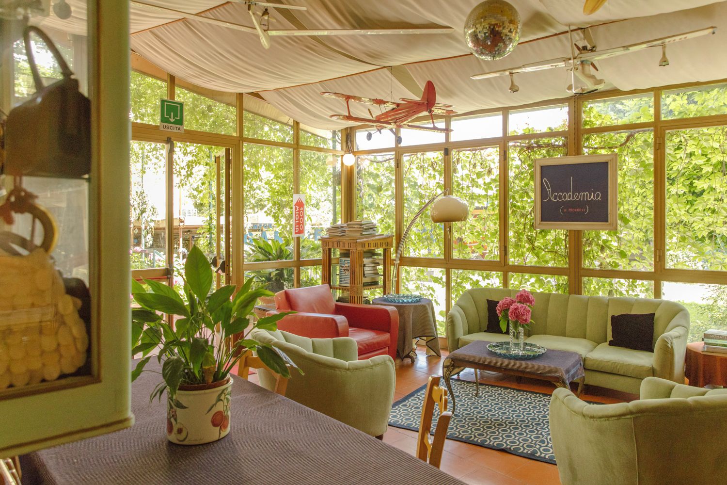 Una habitación amplia con ventanas grandes, un modelo de avión rojo, un sofá verde y una mesa con un jarrón de flores.