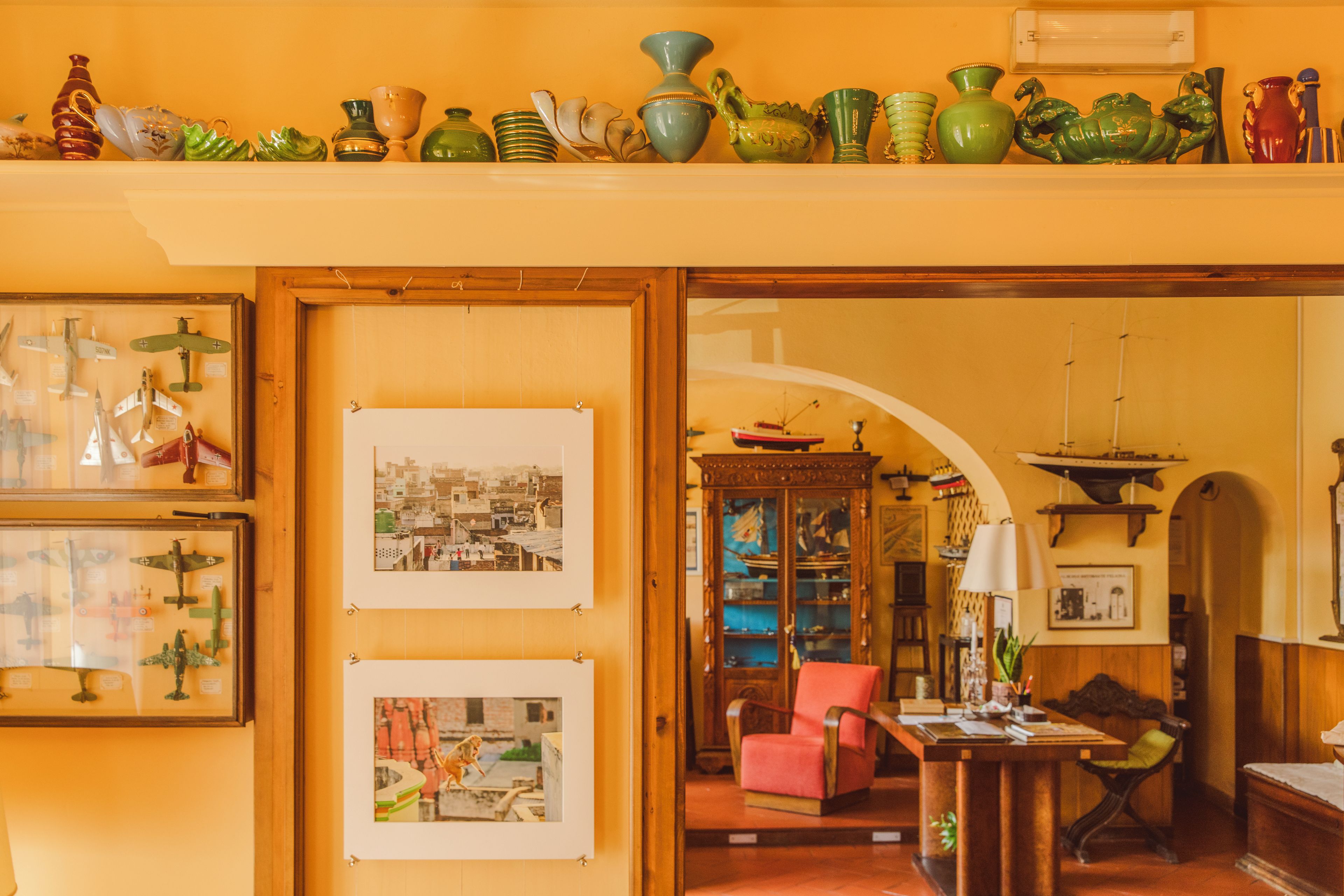 Una habitación con una colección de objetos decorativos en un estante, fotografías enmarcadas en la pared y un escritorio con una silla.