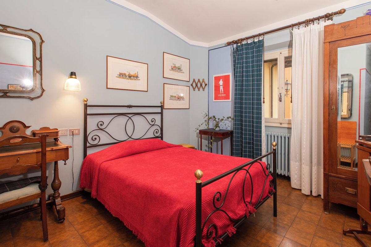 A bedroom with a bed, a desk, a mirror, and framed pictures on the wall.