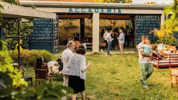 Un espacio al aire libre con mesas y sillas, una valla de madera, un cartel que dice 'ACCADEMIA' y personas cenando.
