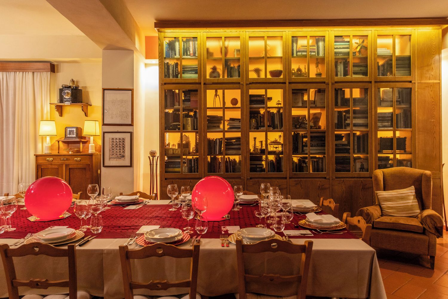Ein Esszimmer mit rotem Tischleinentuch, gedeckt für eine Mahlzeit, und einem großen Schrank mit Glastüren im Hintergrund.