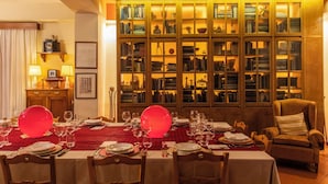 Una sala menjador amb estovatge vermell, preparada per a dinar, i un gran armari exhalador amb portes de vidre al fons.
