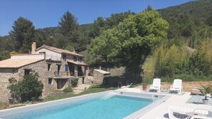 Una villa de piedra con piscina, sillas de descanso y vistas a una ladera boscosa.