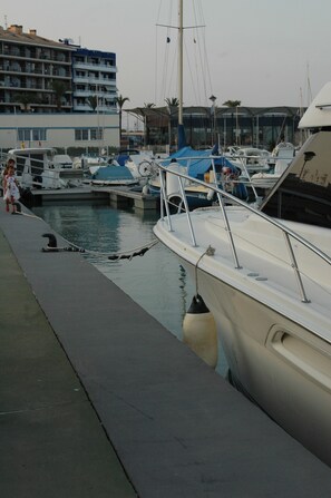 A marina with several boats docked, a building with balconies in the background, and a person in a white dress walking along the dock. - First Line Apartment With Wifi (Benicarlo)