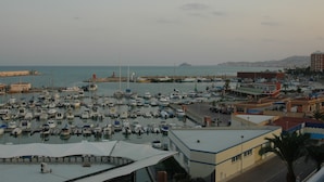 A marina with numerous boats docked, a building with a flat roof, and a distant view of a hilly landscape. - First Line Apartment With Wifi (Benicarlo)