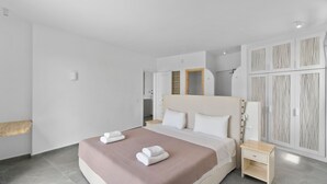 A modern bedroom with a large bed, a nightstand, a wardrobe, and a bathroom visible through an open door. - Seahorse Villa Andros: Beachfront with Private Pool (Kalamitsi, Andros)