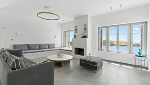 A modern living room with a grey sofa, a round coffee table, and a fireplace. - Seahorse Villa Andros: Beachfront with Private Pool (Kalamitsi, Andros)