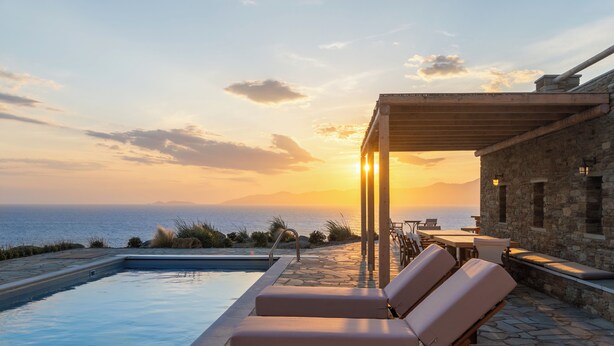 A poolside area with lounge chairs and a table, overlooking the sea at sunset. - Seahorse Villa Andros: Beachfront with Private Pool (Kalamitsi, Andros)