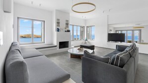 A modern living room with a large gray sectional sofa, a round coffee table, and a flat-screen TV mounted on the wall. - Seahorse Villa Andros: Beachfront with Private Pool (Kalamitsi, Andros)