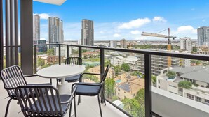 Ein Balkon mit Tisch und Stühlen, der auf eine Skyline mit Hochhäusern und Baukränen blickt.