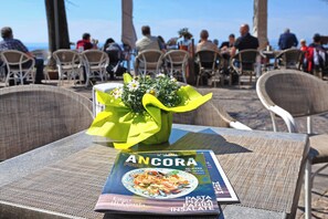 A table with a magazine titled "ANCORA Food Gelateria" and a bouquet of flowers. - Albergo all'Ancora (Garda)